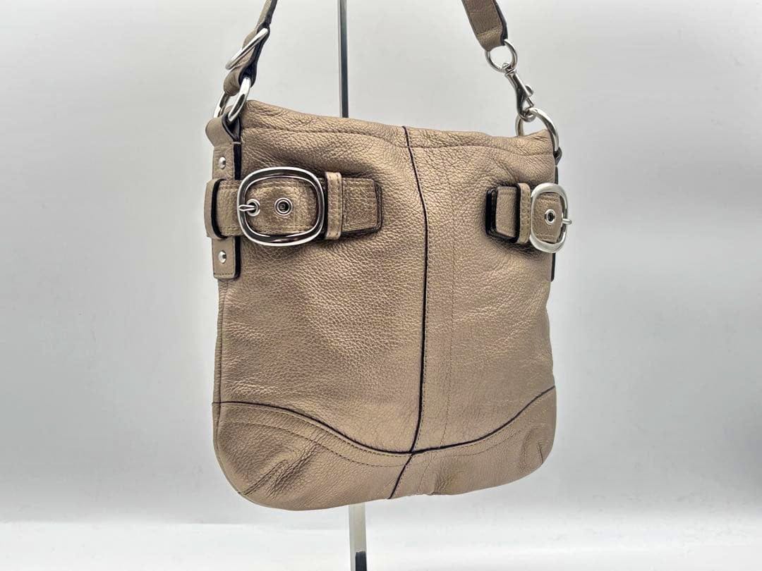 Tan leather COACH sacoche shoulder bag shown from the front with two silver buckles and a short strap.