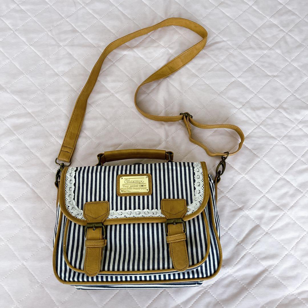 Striped navy-and-white fabric shoulder bag with tan trim, lace detail, buckles, and an adjustable strap on a quilted surface.