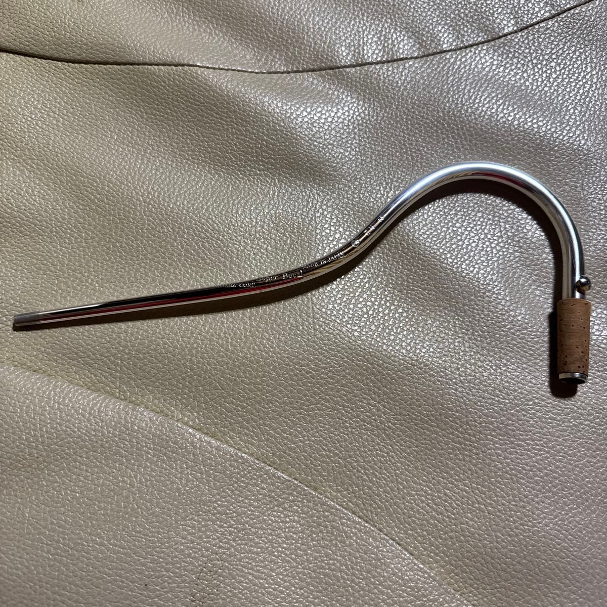 Curved metal bassoon bocal (Yamaha EN2S) with a cork tenon on a leather surface.