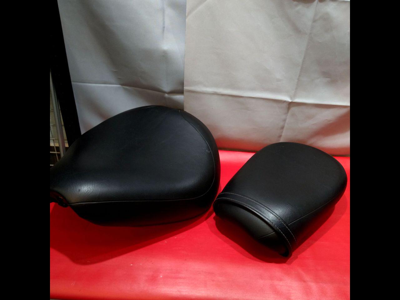 Two black motorcycle seats (rider and passenger) placed on a red surface with a white backdrop.