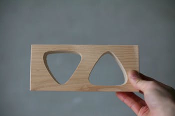 Wooden triangular onigiri mold with two cavities held by a hand against a neutral gray background.