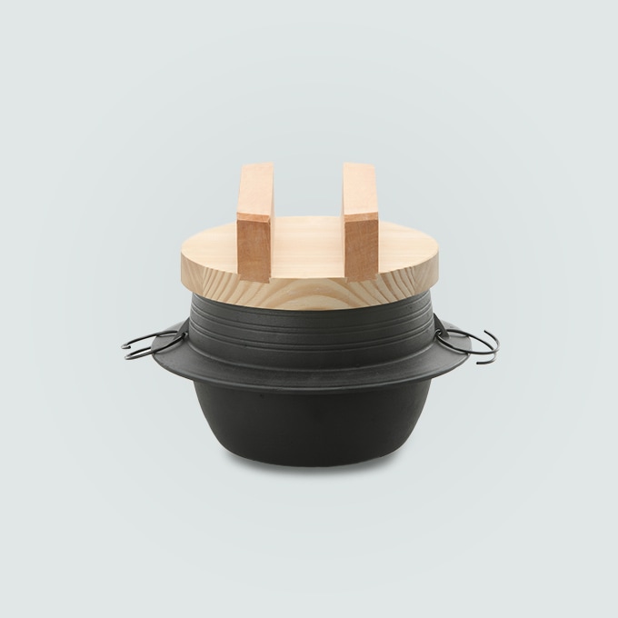 An iron pot with a wooden lid and side handles on a plain background.