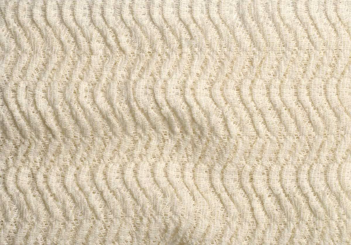 Close-up of cream-colored soft-pile polyester fabric showing a wavy textured pile.