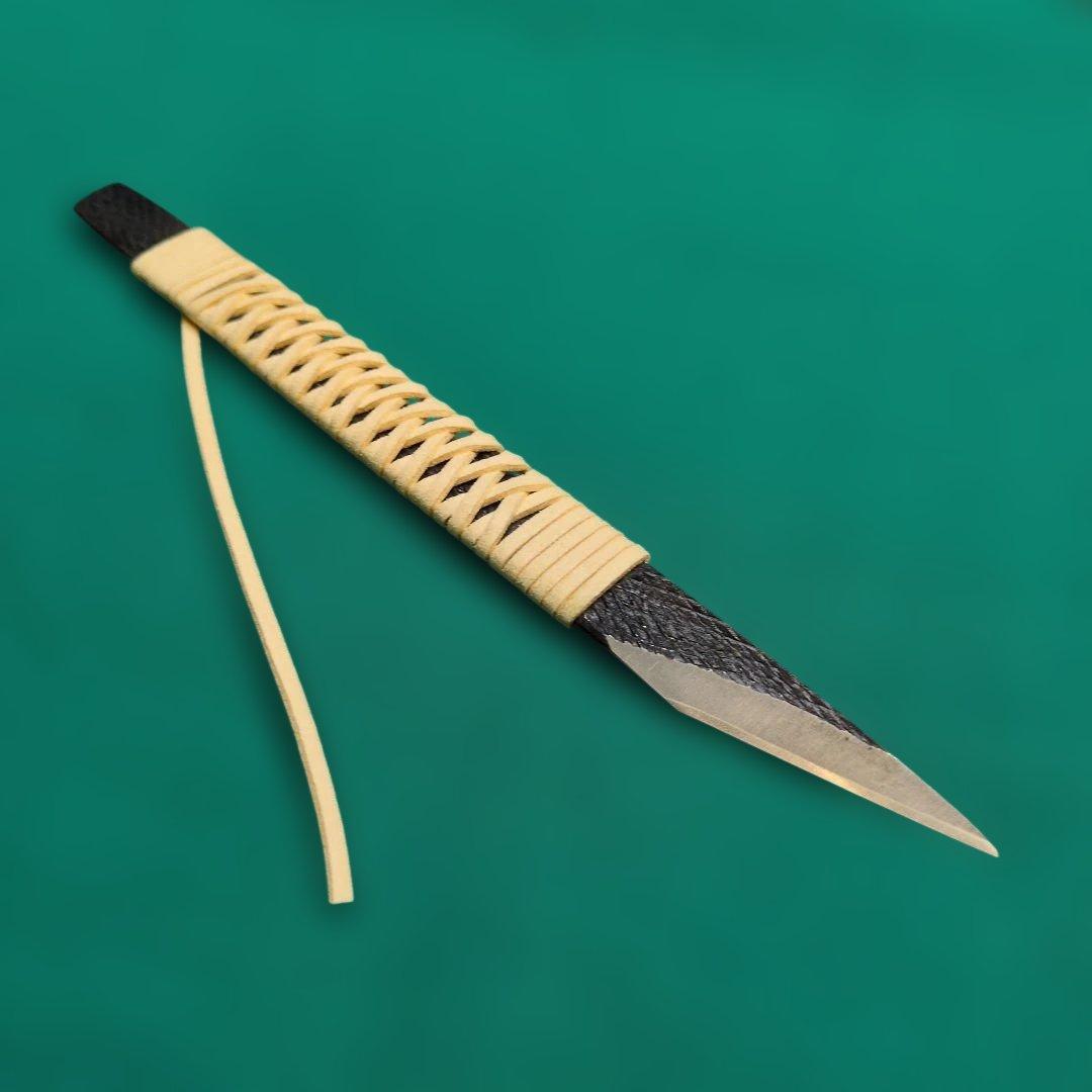 A cut‑out chef knife with a leather‑wrapped handle and narrow 12mm, 180mm blade displayed on a green background.