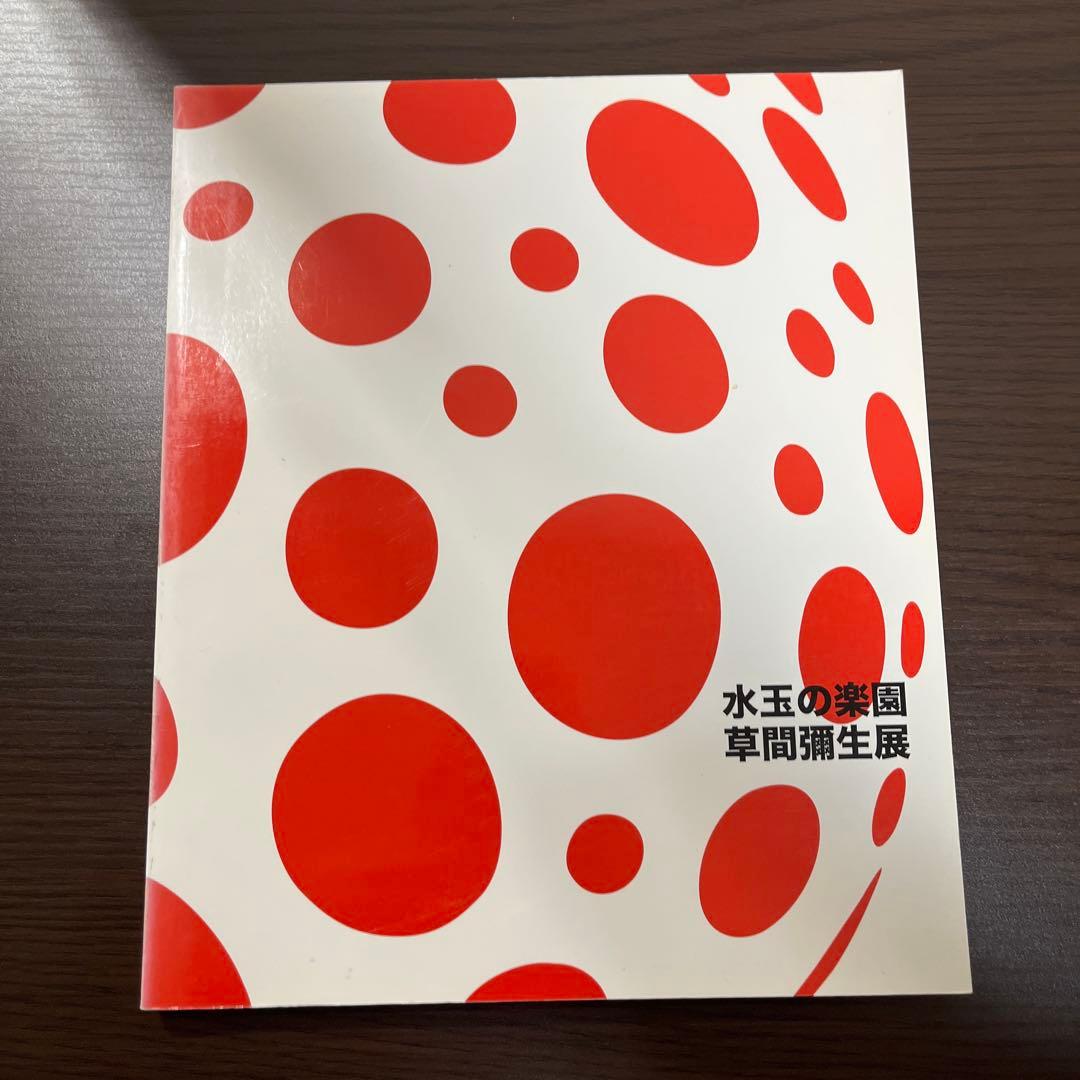 Front cover of the exhibition catalog showing red polka dots on white background and the Japanese title 水玉の楽園 草間彌生展.
