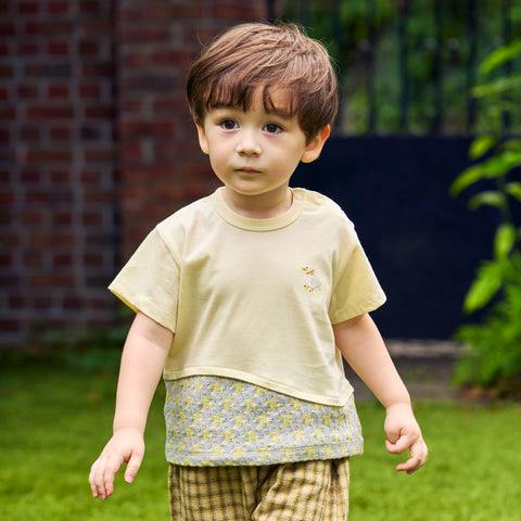 A child wearing a yellow children's T-shirt with a small duck embroidery on the chest.