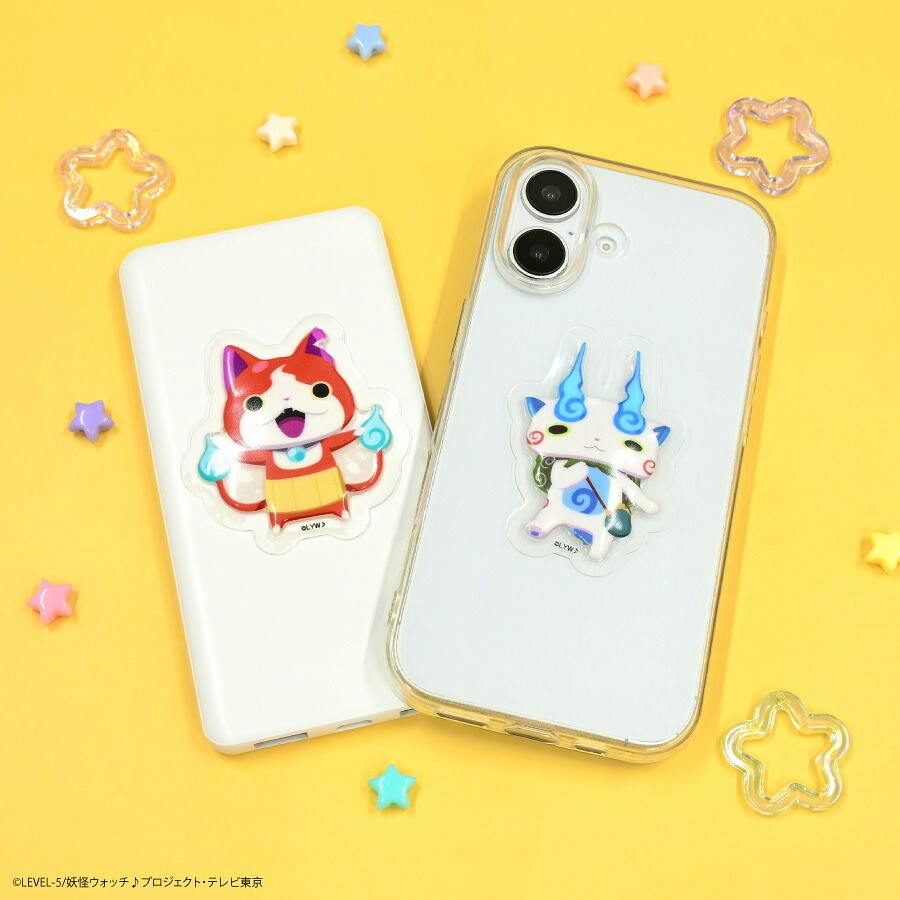 Two smartphones on a yellow background, each decorated with a puffy Yo-kai Watch character sticker (Jibanyan on one and Komasan on the other) with small star-shaped decorations around them.