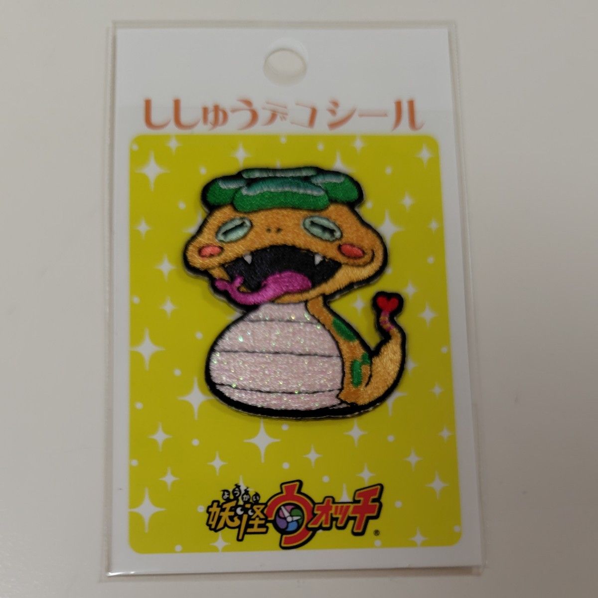 Packaged embroidered iron-on patch of the Tsuchinoko character from Yokai Watch on a yellow backing card.