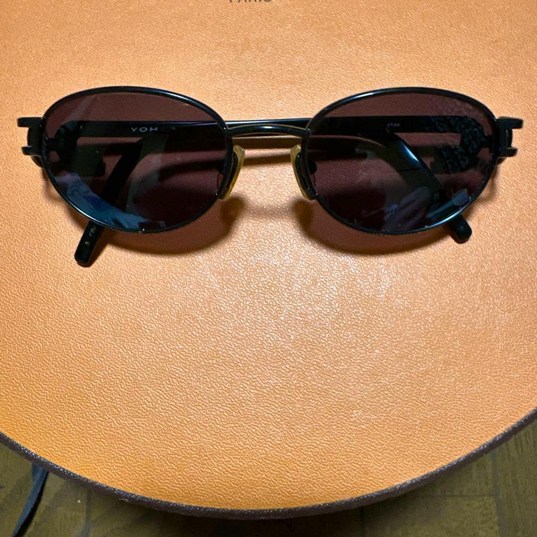 Black sunglasses with dark oval lenses shown resting on an orange surface.