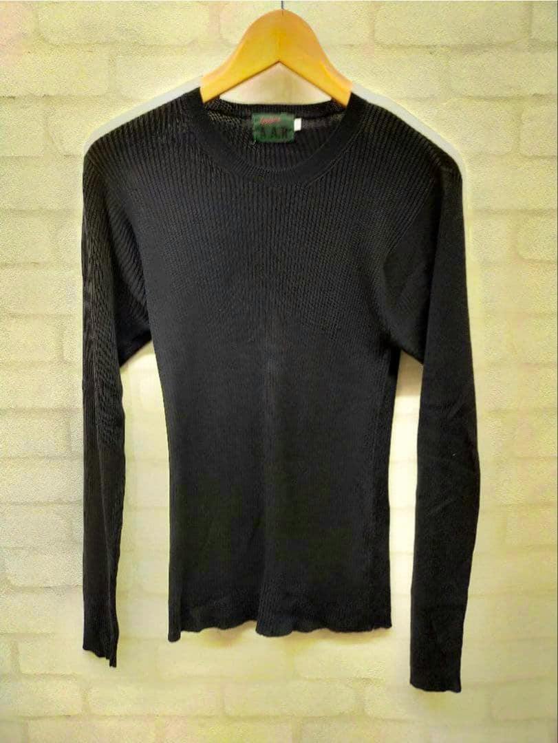 Black long-sleeve ribbed knit top hanging on a wooden hanger against a light brick wall.