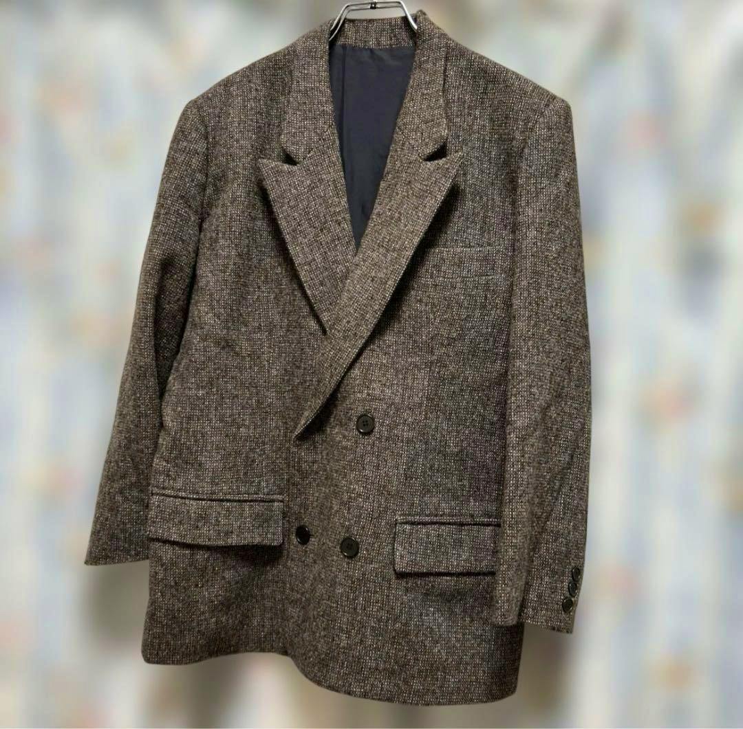 A brown-beige double-breasted men's wool jacket hanging on a hanger against a blurred background.