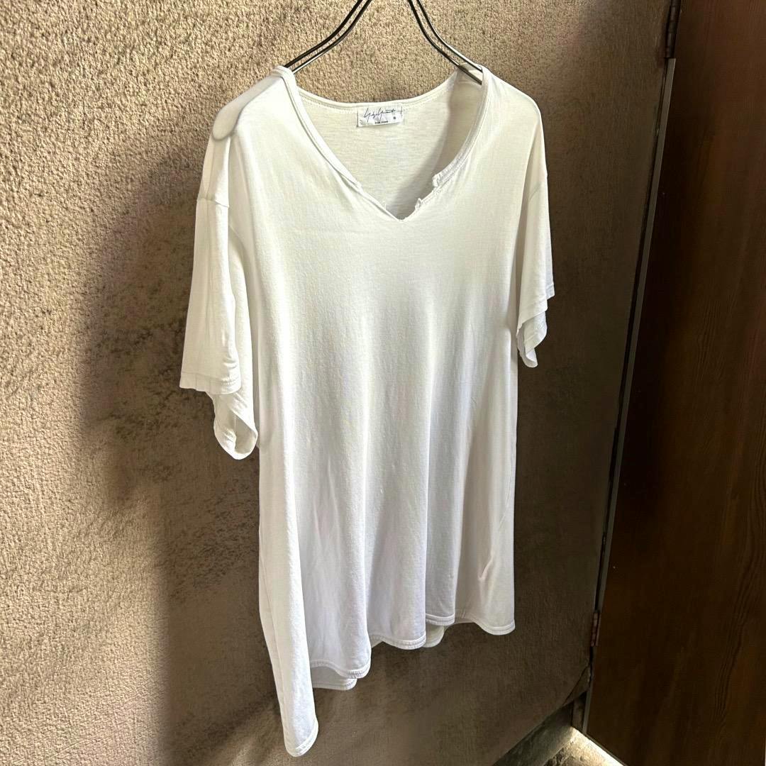 White Yohji Yamamoto POUR HOMME 18SS damaged T-shirt hanging on a hanger against a textured wall.