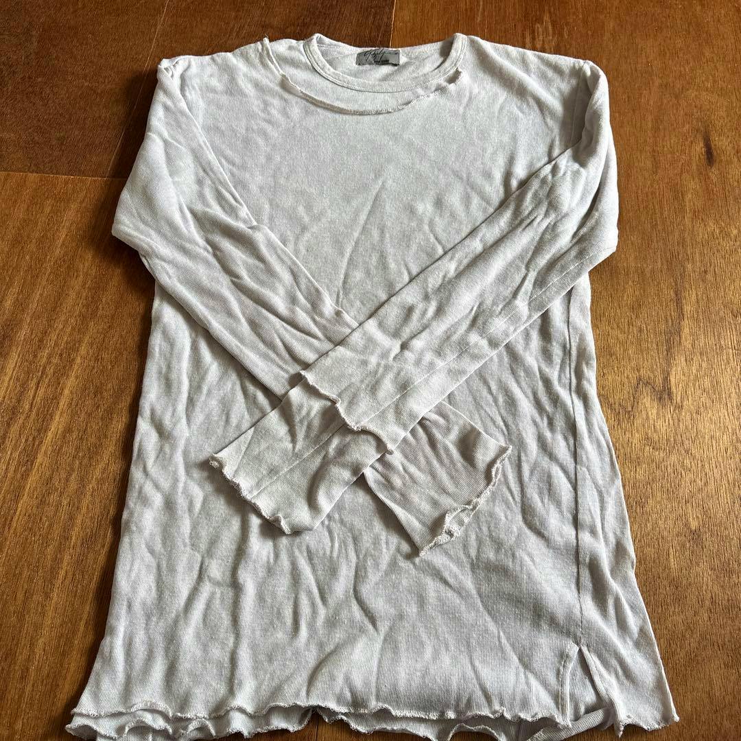 Flat-lay photo of a light-colored long-sleeve cotton men's shirt (yohji yamamoto pour homme) laid on a wooden floor.