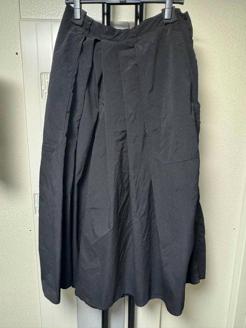 Black polyester hakama-style men's pants hanging on a hanger against a light wall, front view.