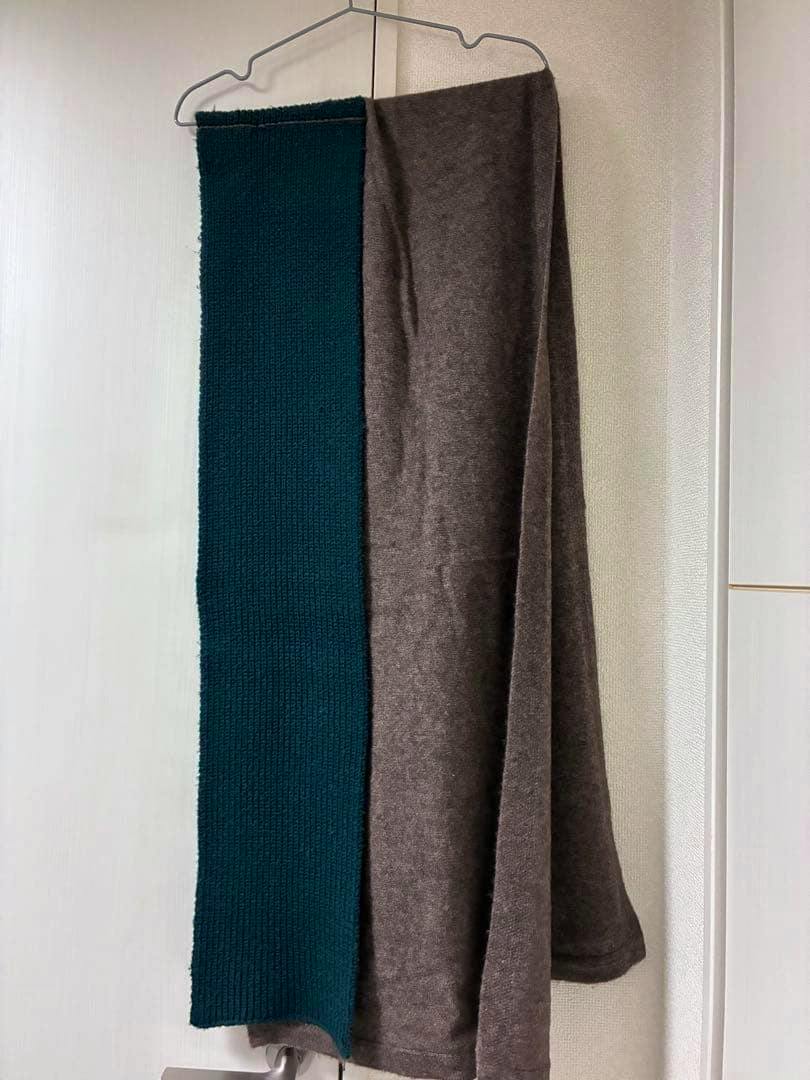 A bicolor knit scarf in dark green and brown hanging on a hanger against a light wall.