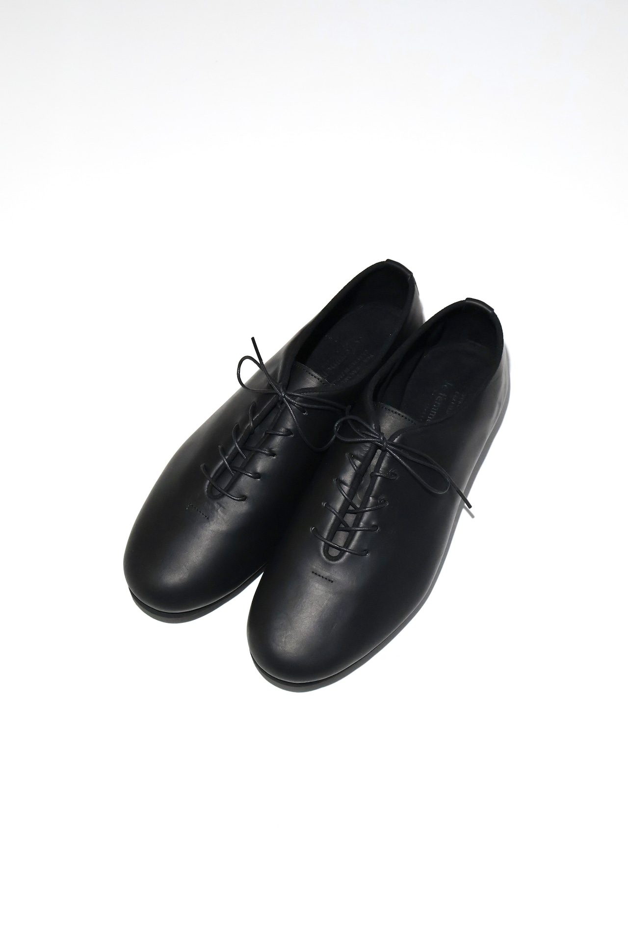 Pair of black leather jazz flat shoes with laces photographed on a white background.