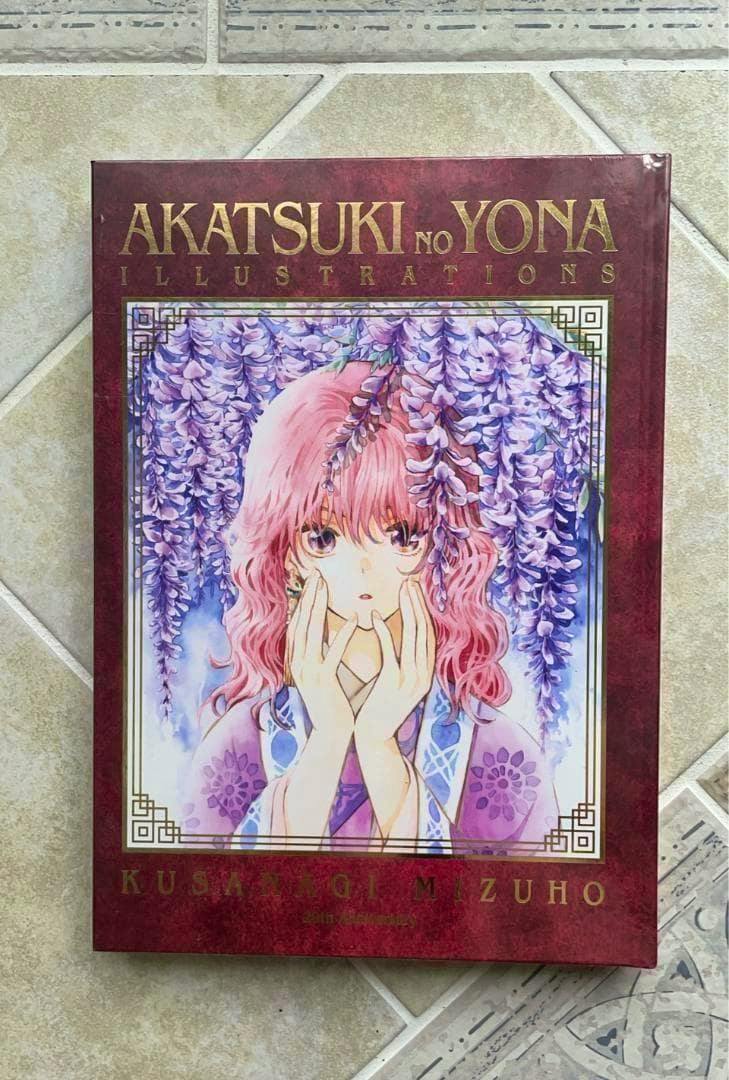 Front cover of the Akatsuki no Yona illustration book showing a pink-haired character framed by hanging purple flowers and the title "AKATSUKI NO YONA".