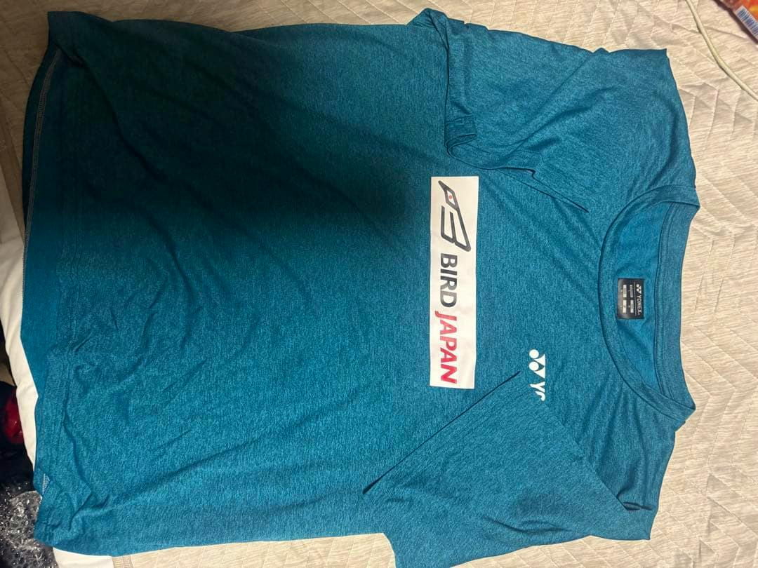 Teal Yonex badminton T-shirt laid flat showing the front with a BIRD JAPAN graphic and Yonex logo.