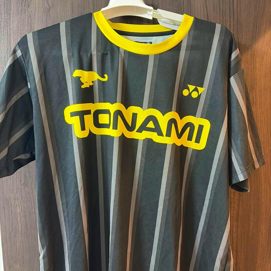 Front view of a Yonex Tonami badminton uniform shirt with yellow TONAMI logo hanging on a hanger.