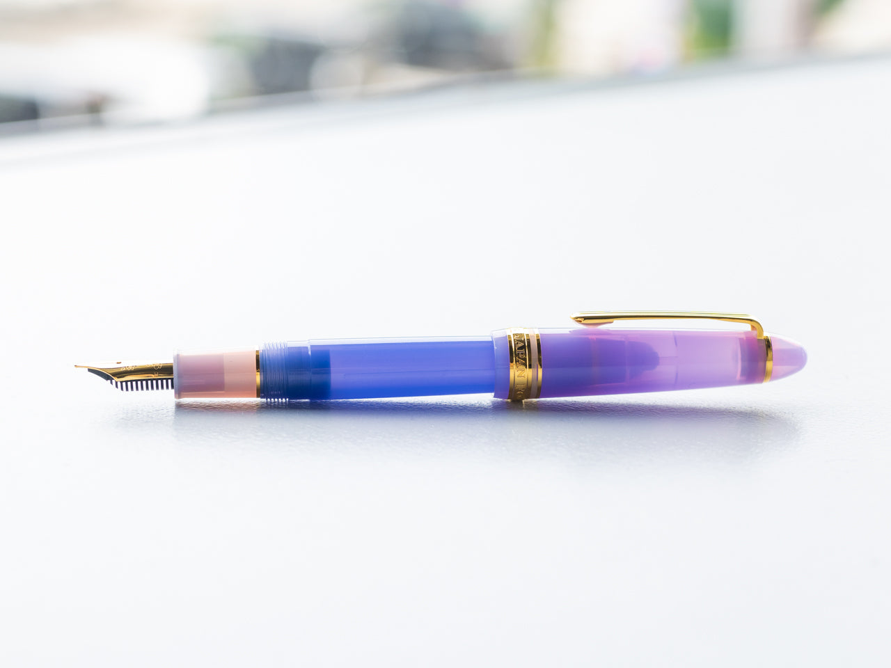 A purple and blue translucent fountain pen with gold trim and exposed nib lying horizontally.