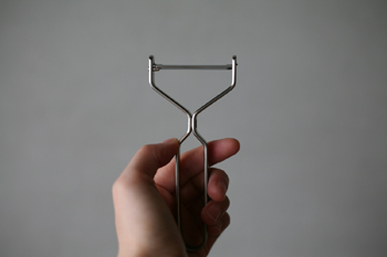 A stainless steel Y-shaped peeler held in a hand against a plain gray background.