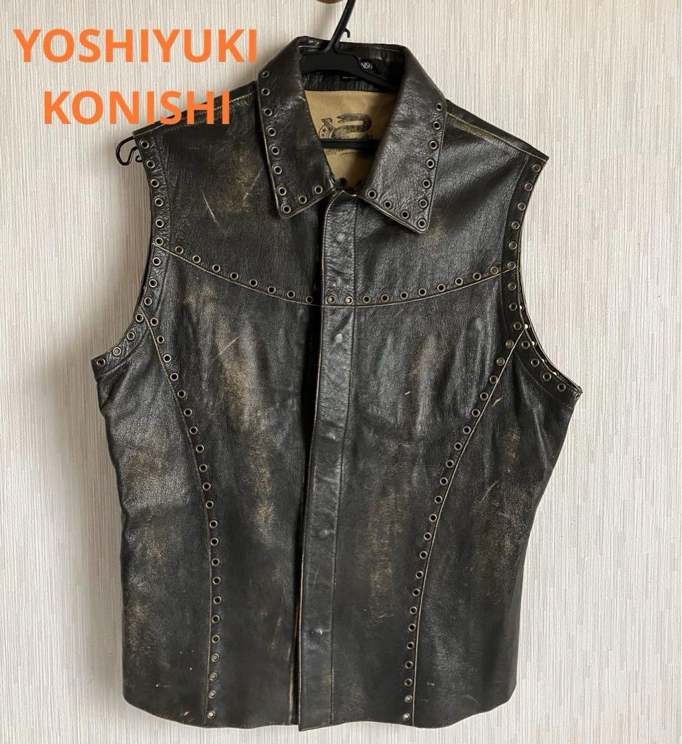 Front view of a Yoshiyuki Konishi goat leather sleeveless vest with metal eyelets on the collar and seams, hanging on a hanger against a light wall.