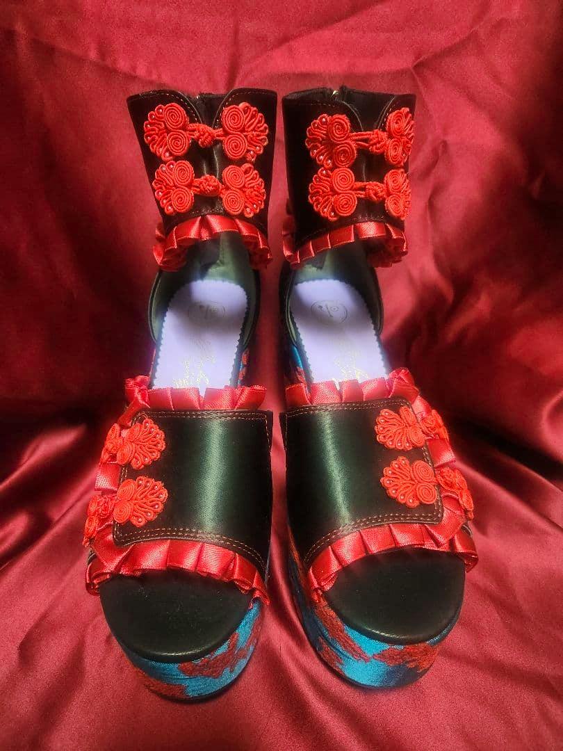 Pair of Yosuke China thick-soled sandals in green and red shown from the front on a red fabric background.