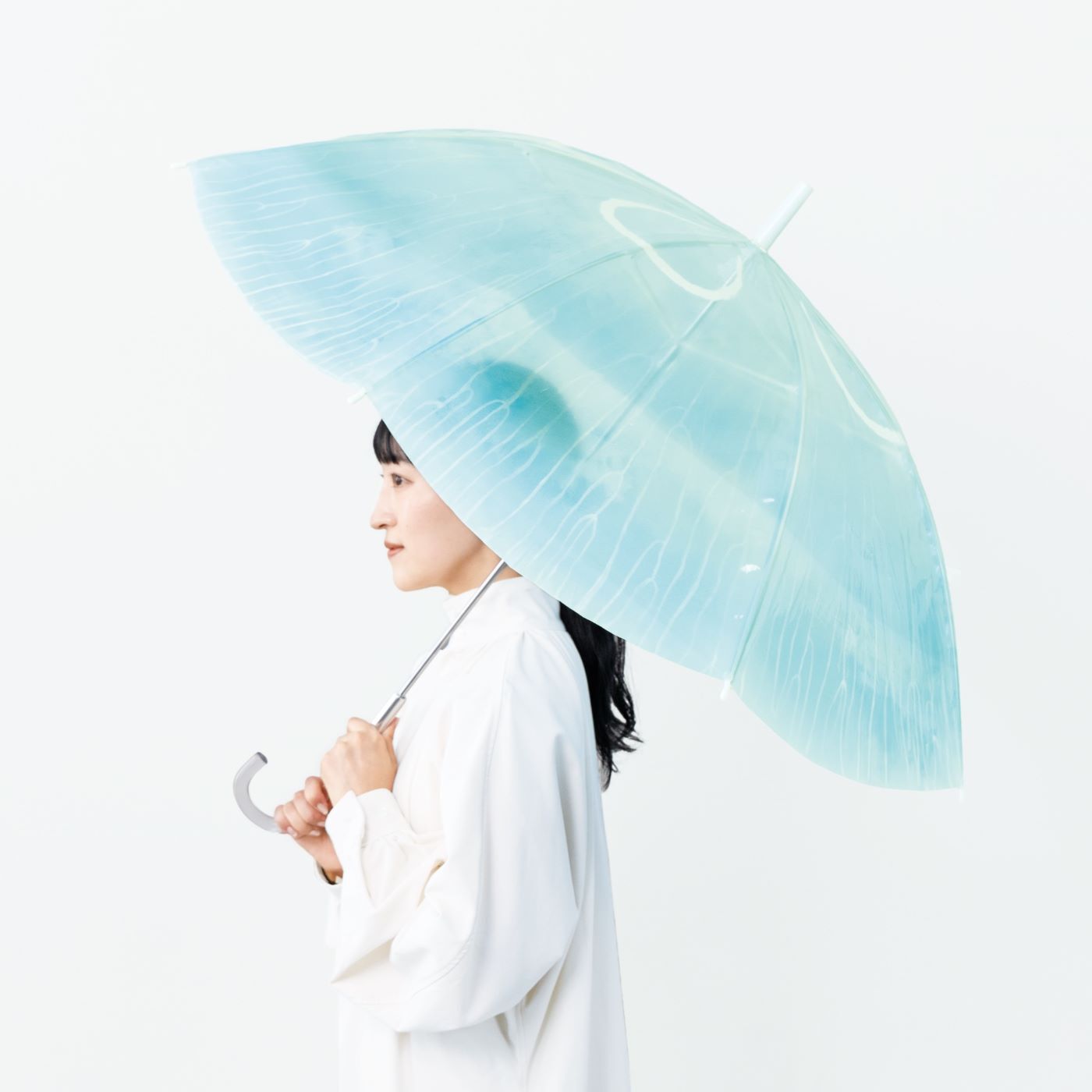 Side profile of a person holding a translucent pale blue jellyfish-patterned umbrella.