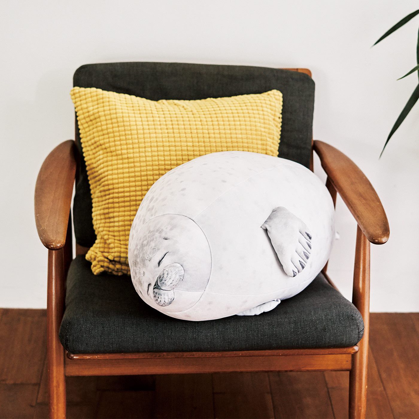 A round seal-shaped cushion placed on a wooden armchair with a yellow textured pillow behind it.