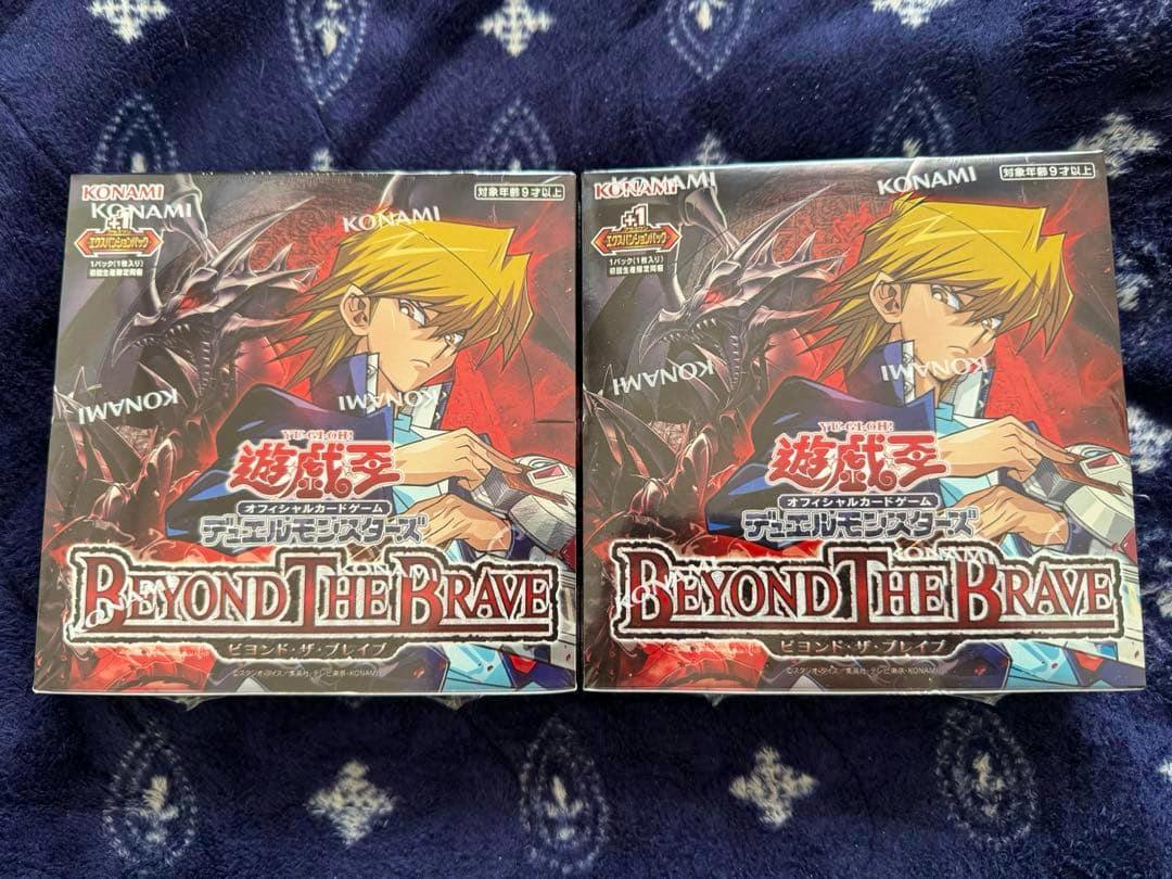 Two shrink-wrapped "BEYOND THE BRAVE" Yu-Gi-Oh booster boxes shown side by side on a patterned dark cloth.