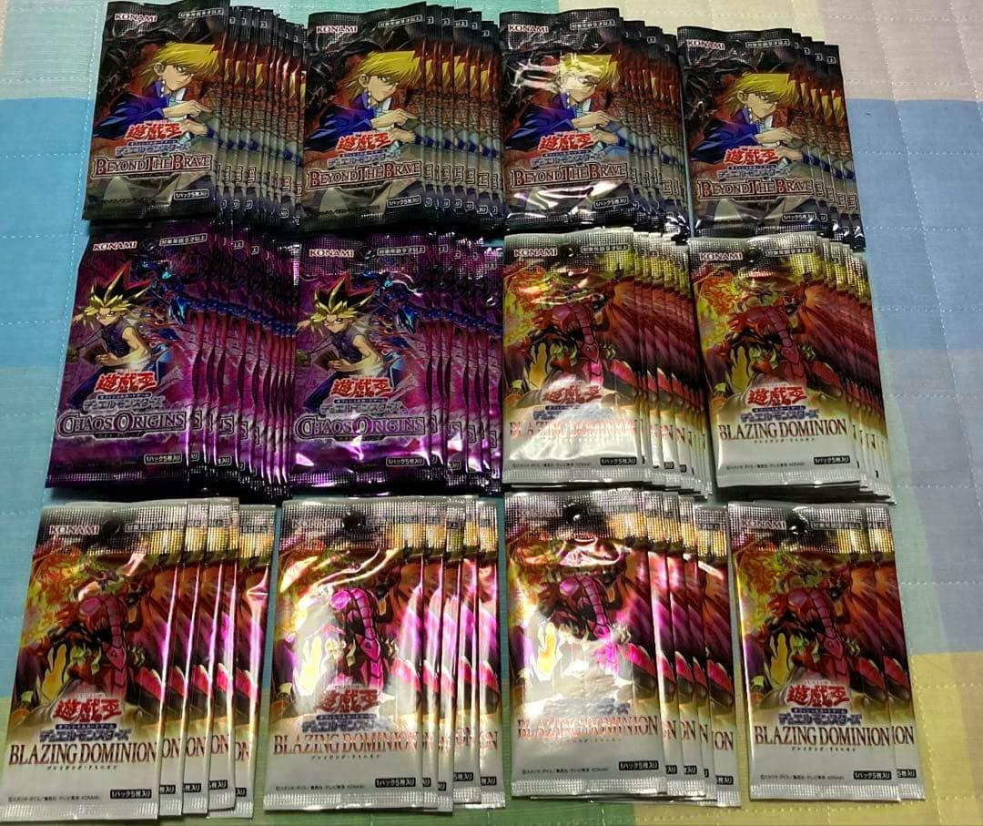 Multiple Yu-Gi-Oh! trading card booster packs (Beyond the Brave, Chaos Origins, and Blazing Dominion) arranged in rows on a surface.