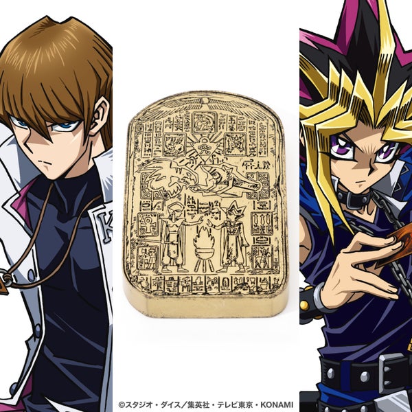 A zinc-alloy paperweight modeled after "Lost Memories of the Pharaoh" with engraved Egyptian-style markings, shown centered between two Yu-Gi-Oh character illustrations.