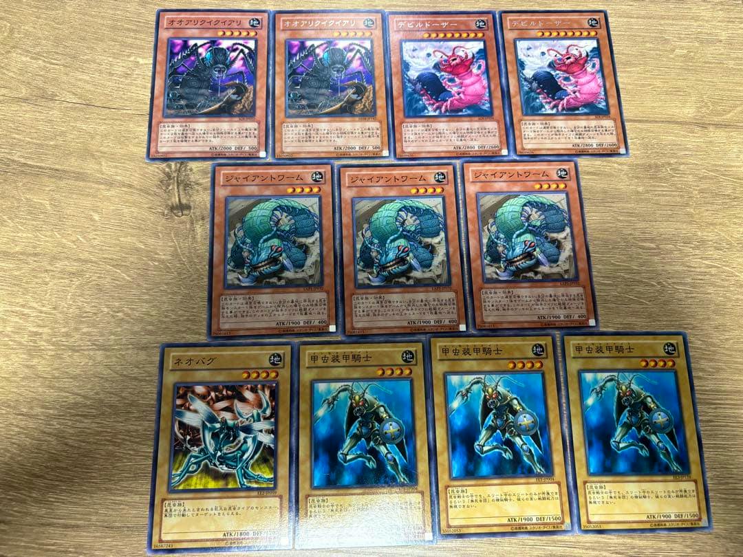 Twelve Yu-Gi-Oh trading cards on a wooden surface, showing Devil Dozer and other insect-type monster cards.