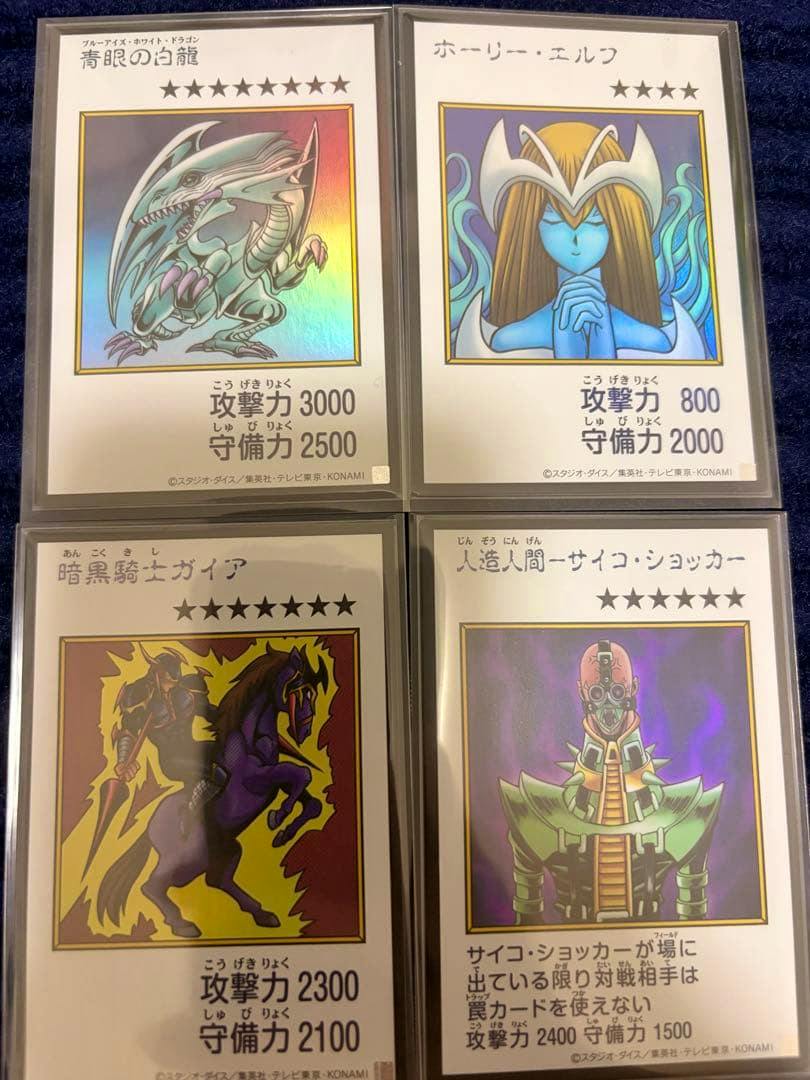 Four Japanese Yu-Gi-Oh trading cards in protective sleeves arranged in a 2x2 grid on a dark blue background.