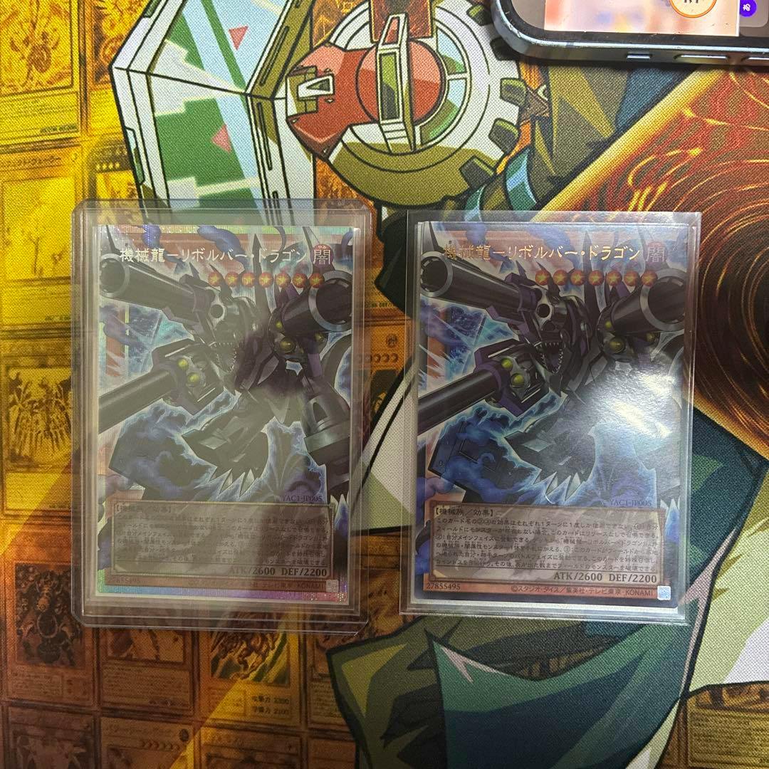 Two 機械龍－リボルバー・ドラゴン (Revolver Dragon) Yu‑Gi‑Oh trading cards in protective sleeves shown side by side on a playmat.