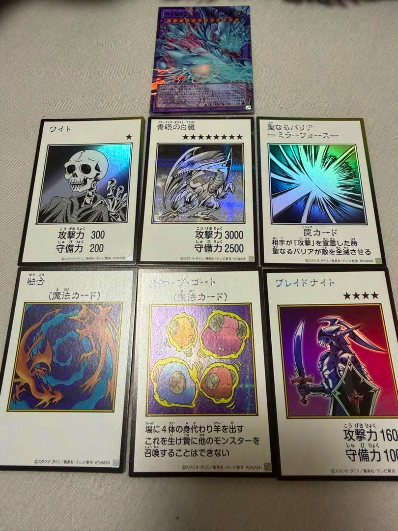 A set of Yu-Gi-Oh trading cards laid out on a surface, showing a monochrome Blue-Eyes White Dragon card among other cards.