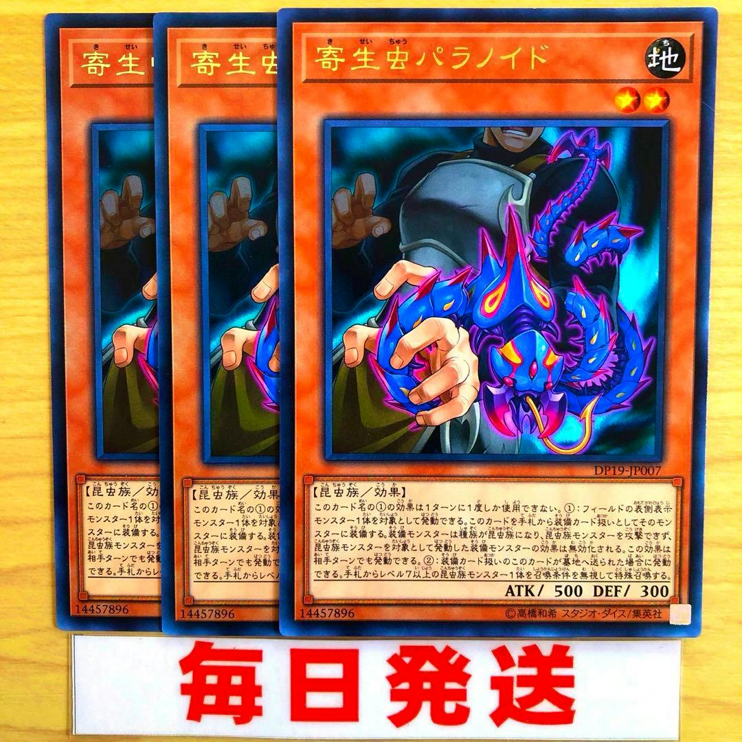 Three Japanese Yu-Gi-Oh trading cards titled 「寄生虫パラノイド」 arranged overlapping on a wooden background above a sign reading 毎日発送.