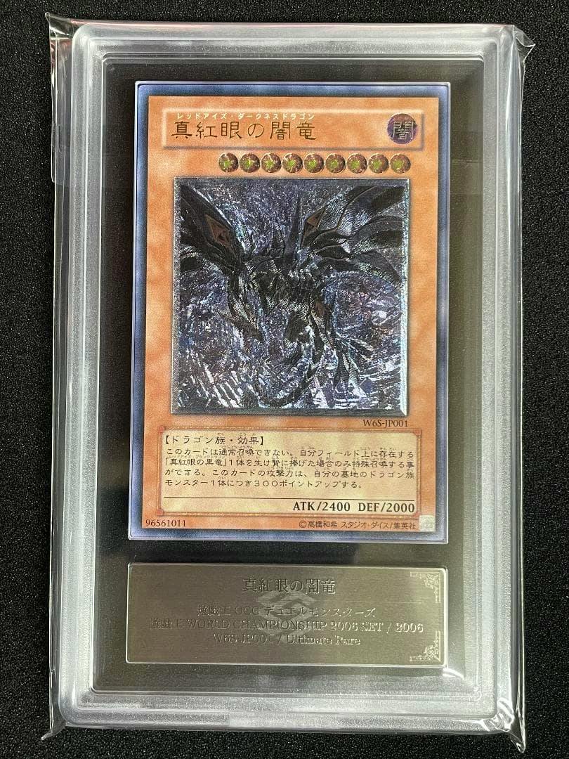 Front of the trading card '真紅眼の闇竜 W6S-JP001' shown inside a clear plastic grading slab, displaying the card artwork and a metal nameplate.