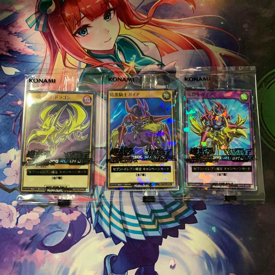 Three Konami-sealed Yu-Gi-Oh Rush Duel campaign trading cards in clear plastic sleeves on a colorful anime playmat.