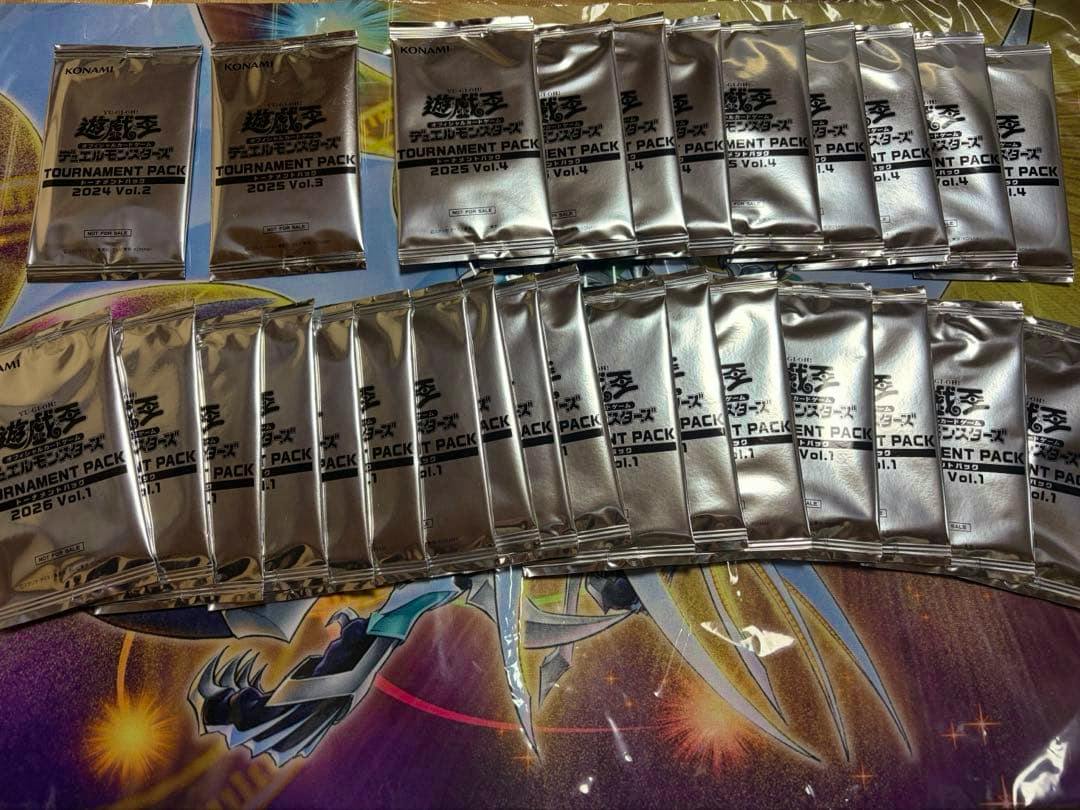 Sealed silver foil packs labeled "遊戯王 / Tournament Pack" (Yu-Gi-Oh) laid out on a playmat.