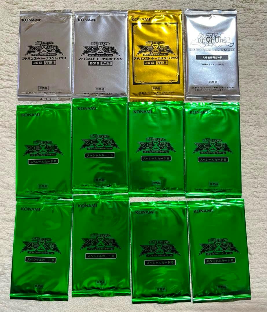 Fronts of twelve sealed Yu-Gi-Oh tournament card booster packs in silver, gold, and green foil arranged on a textured surface.