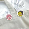 Photo of two round acrylic hair clips with character faces clipped to a light-colored garment.