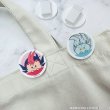 Photo of two round acrylic hair clips showing pink and blue chibi character faces clipped to a light-colored fabric.