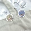 Photograph of two round acrylic hair clips featuring chibi character faces clipped to a light-colored garment.