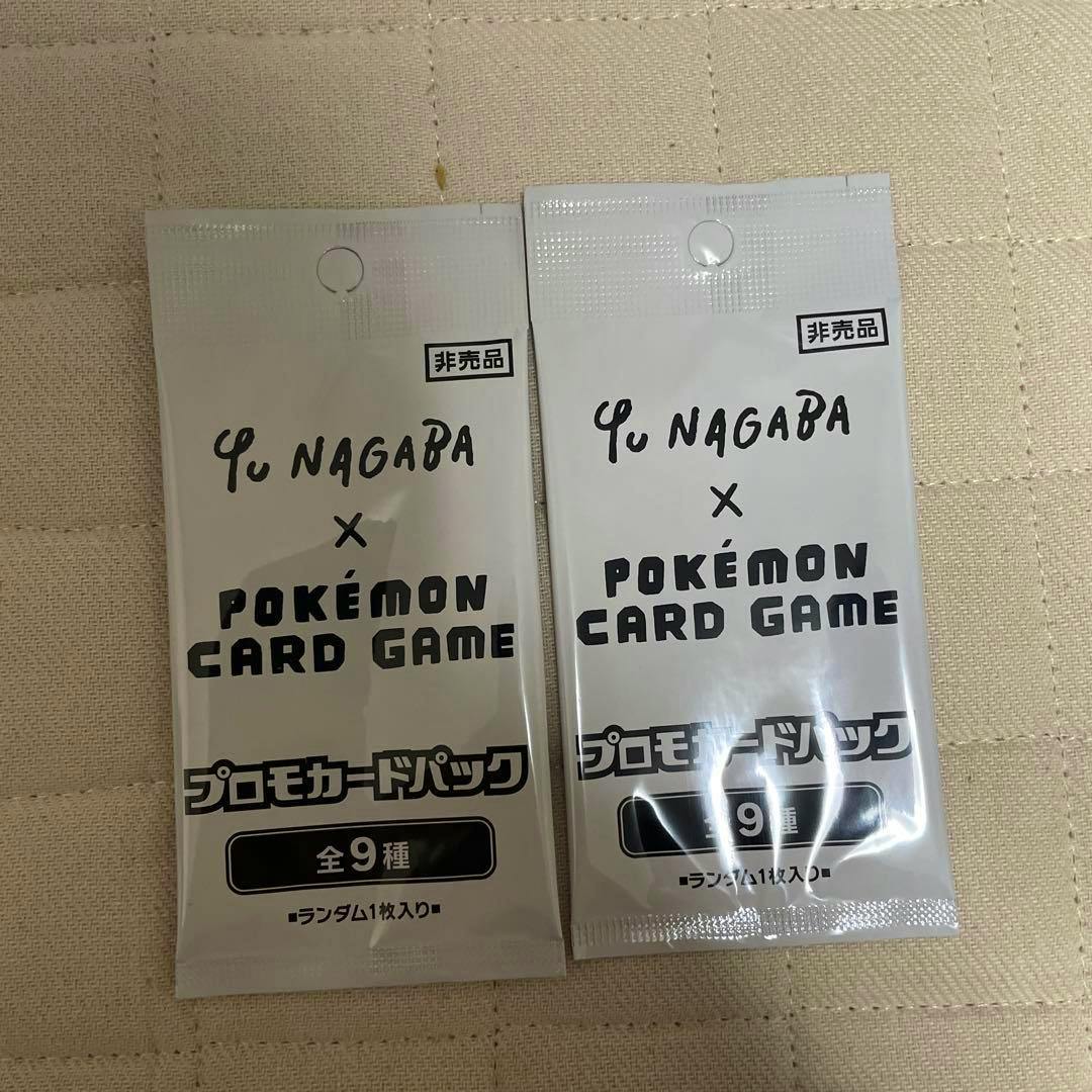 Two sealed Yu Nagaba × Pokémon Card Game promo card packs placed on a beige quilted surface.