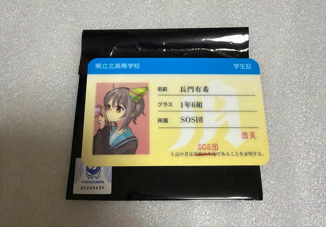 Student-ID–style photocard of 長門有希 from 涼宮ハルヒの憂鬱 showing her portrait and school information, placed on a black sleeve on a light textured surface.