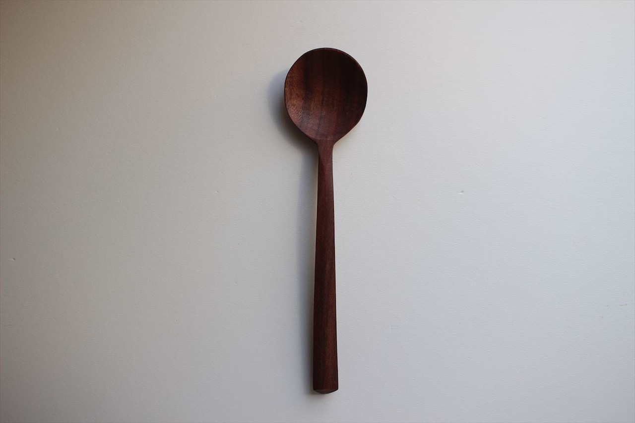 A black walnut round wooden spoon lying flat on a light background.