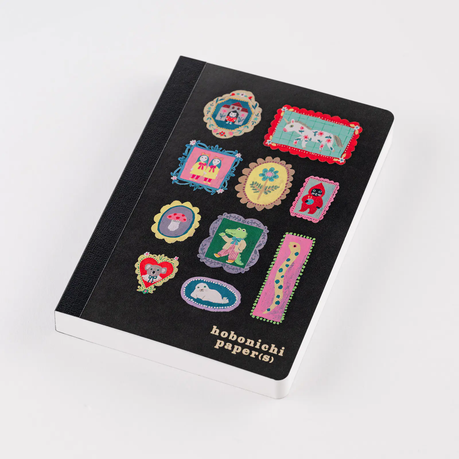A black Hobonichi Paper(s) notebook with colorful illustrated sticker-like designs on the cover and the words "hobonichi paper(s)" printed near the bottom.