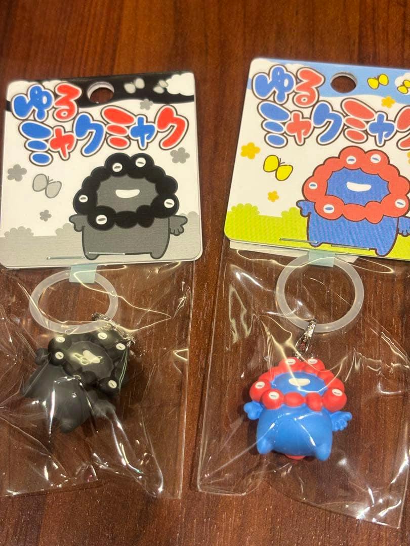 Two packaged ゆるミャクミャク mascot keychains (one black, one blue with red) displayed on a wooden surface.