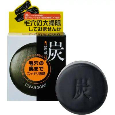 A round black charcoal face soap bar embossed with a Japanese character, displayed next to its product box.